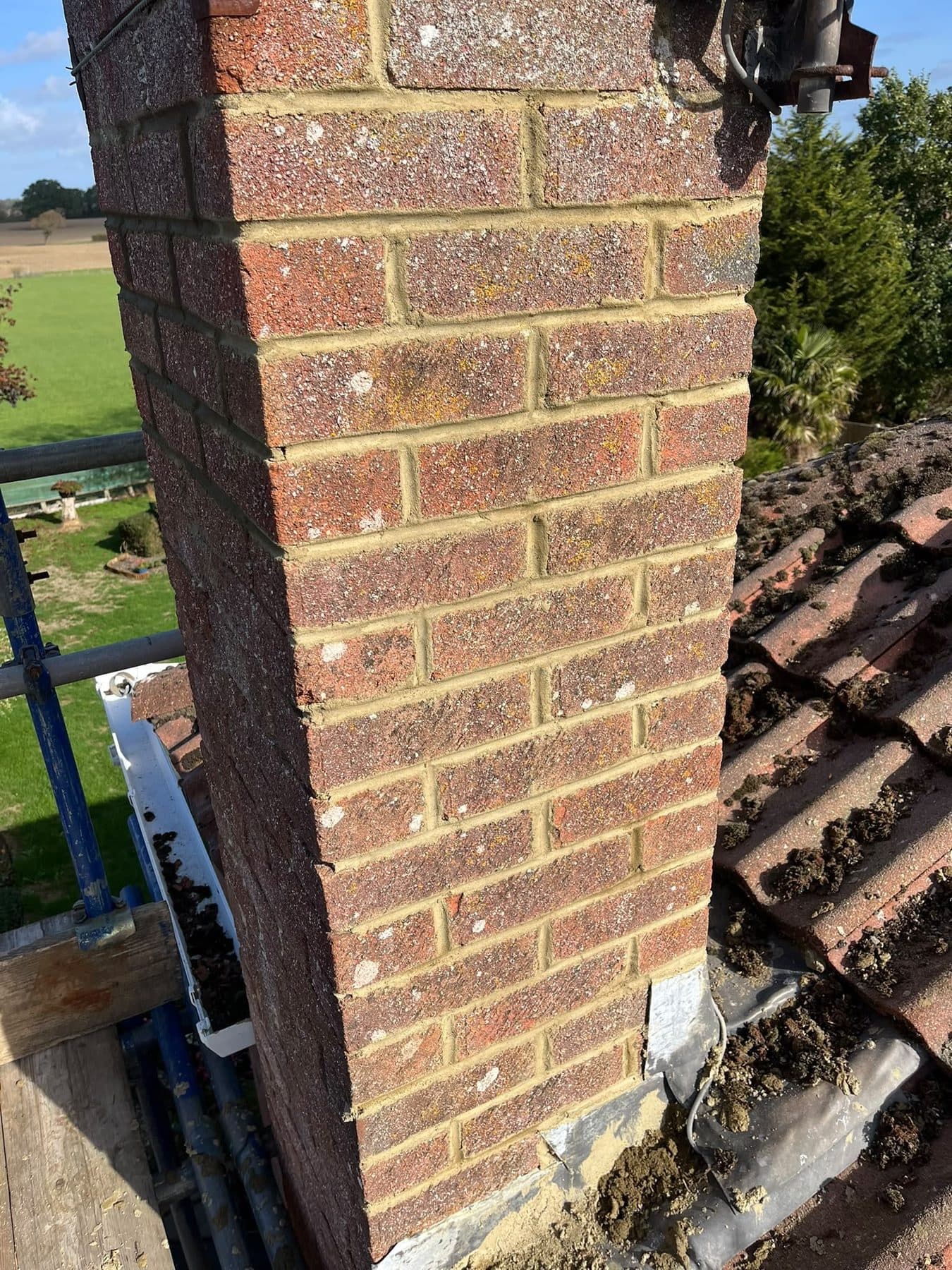 A brick chimney with the tiles beside it lifted and its old flashing coming out