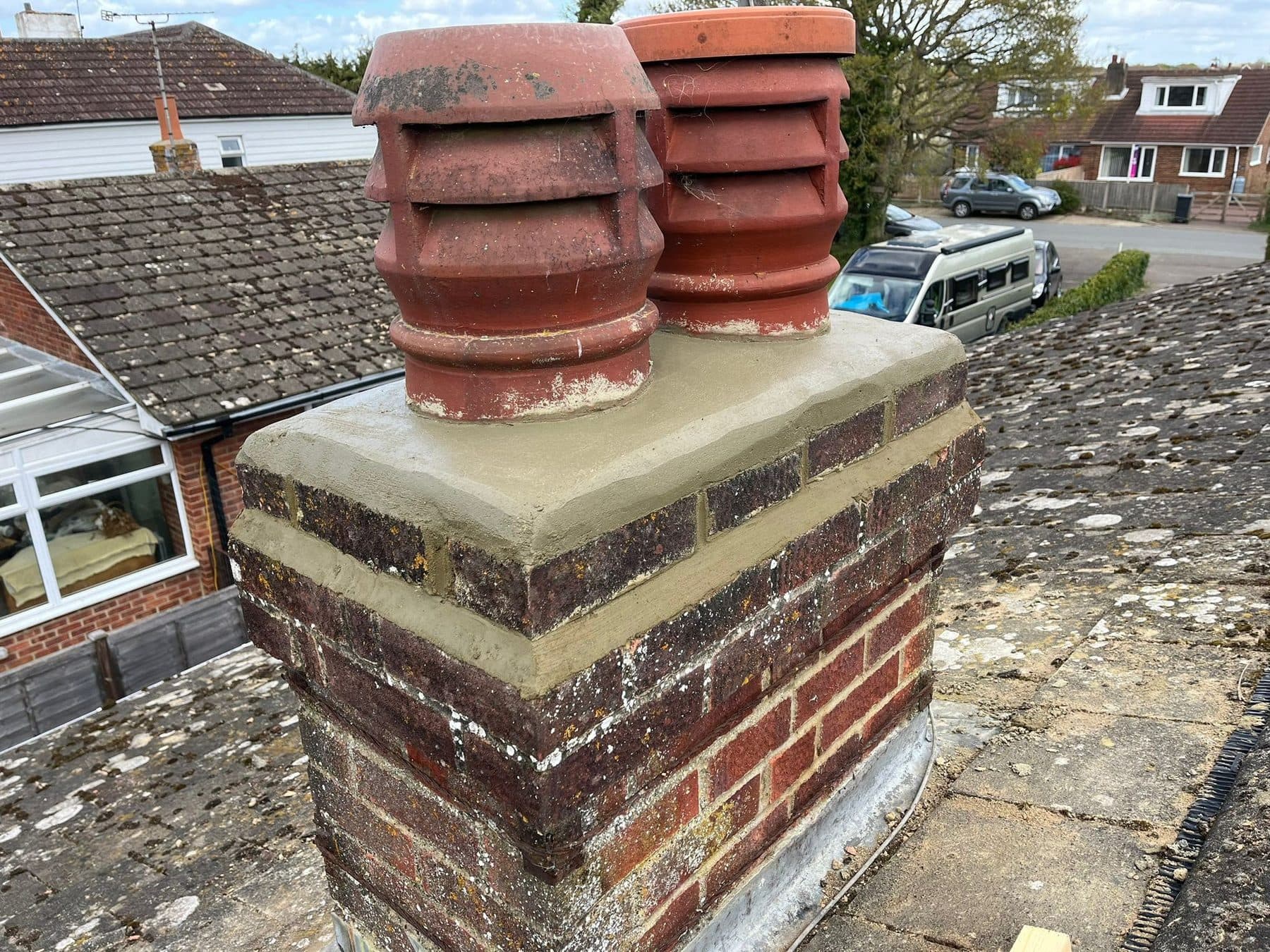 A brick chimney stack with a fresh cement top and two terracotta pots