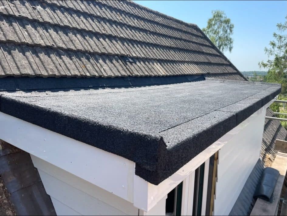 The felt flat roof and white fascia of a dormer, below a concrete tiled roof