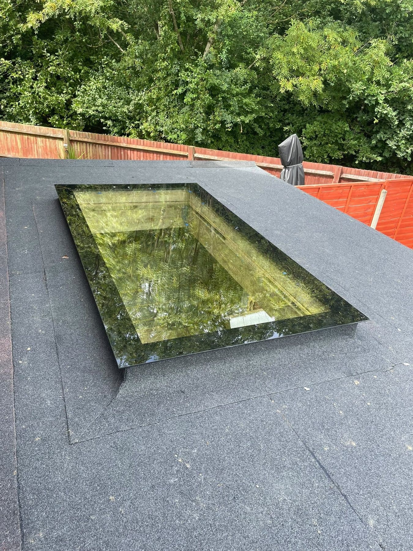 A flat roof in grey mineral felt with a glass rooflight set into it