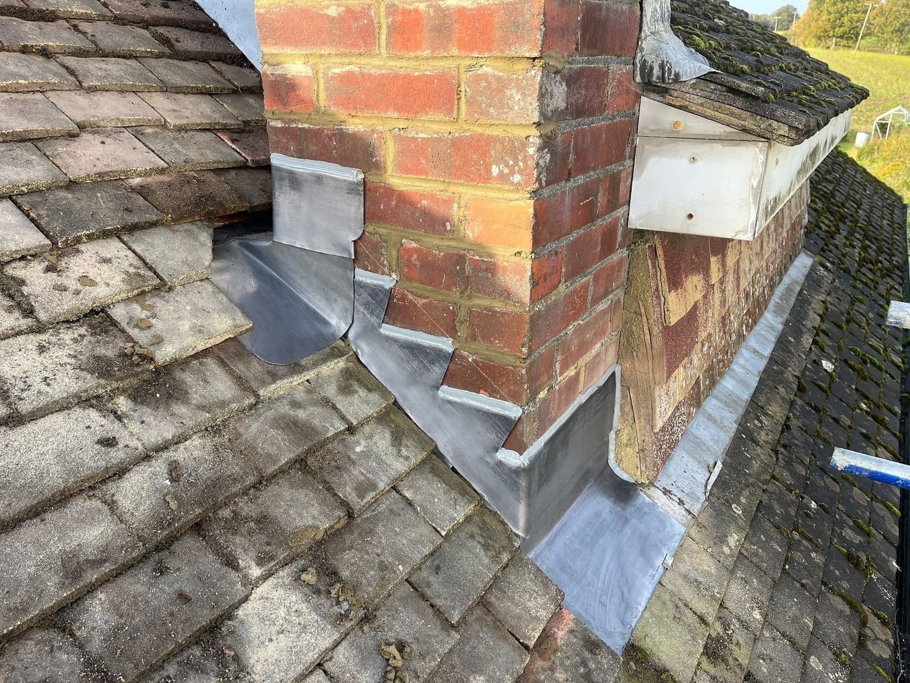 New lead flashing stepped down the side of a brick chimney where it meets the tiles