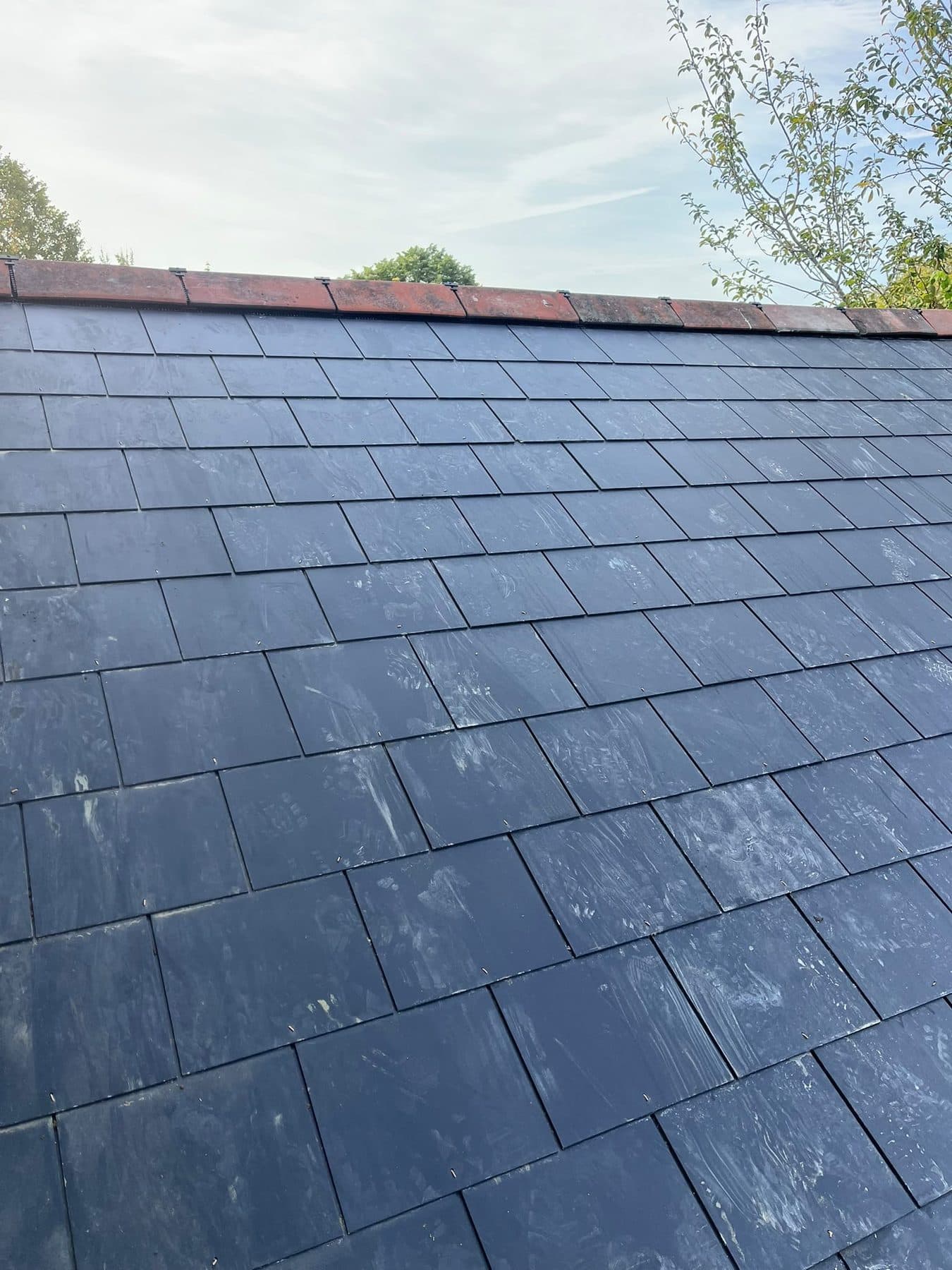 A pitched roof covered in new dark slates, with a clay ridge along the top