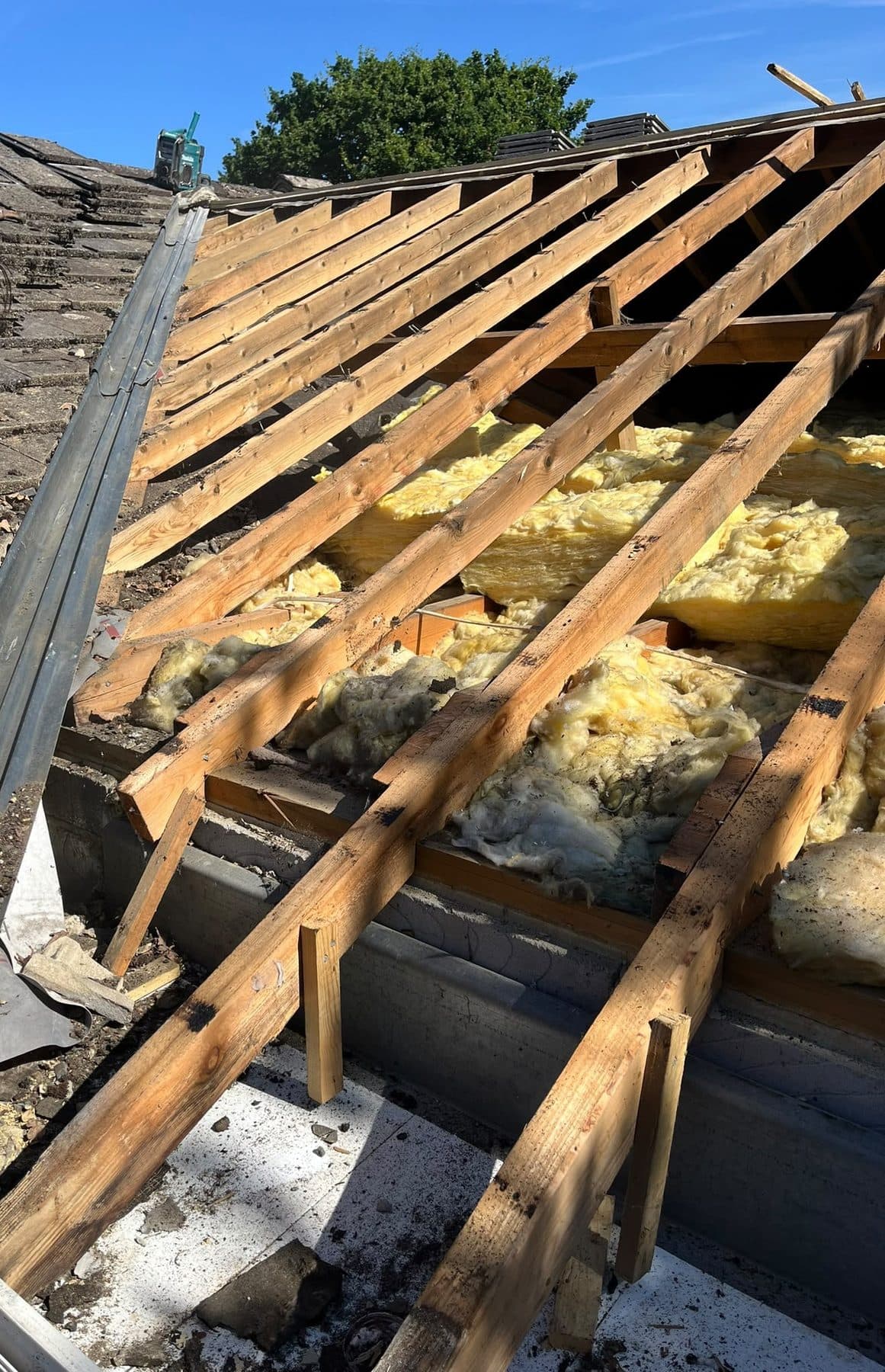A roof stripped down to its rafters, with the loft insulation showing between them