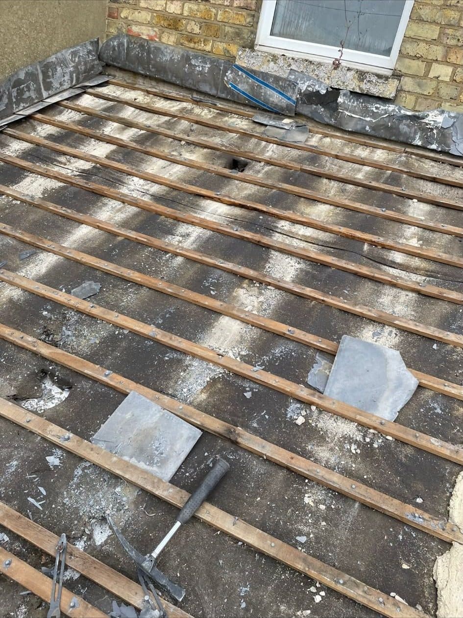 A roof stripped of its old slates, down to the old battens, against a brick wall