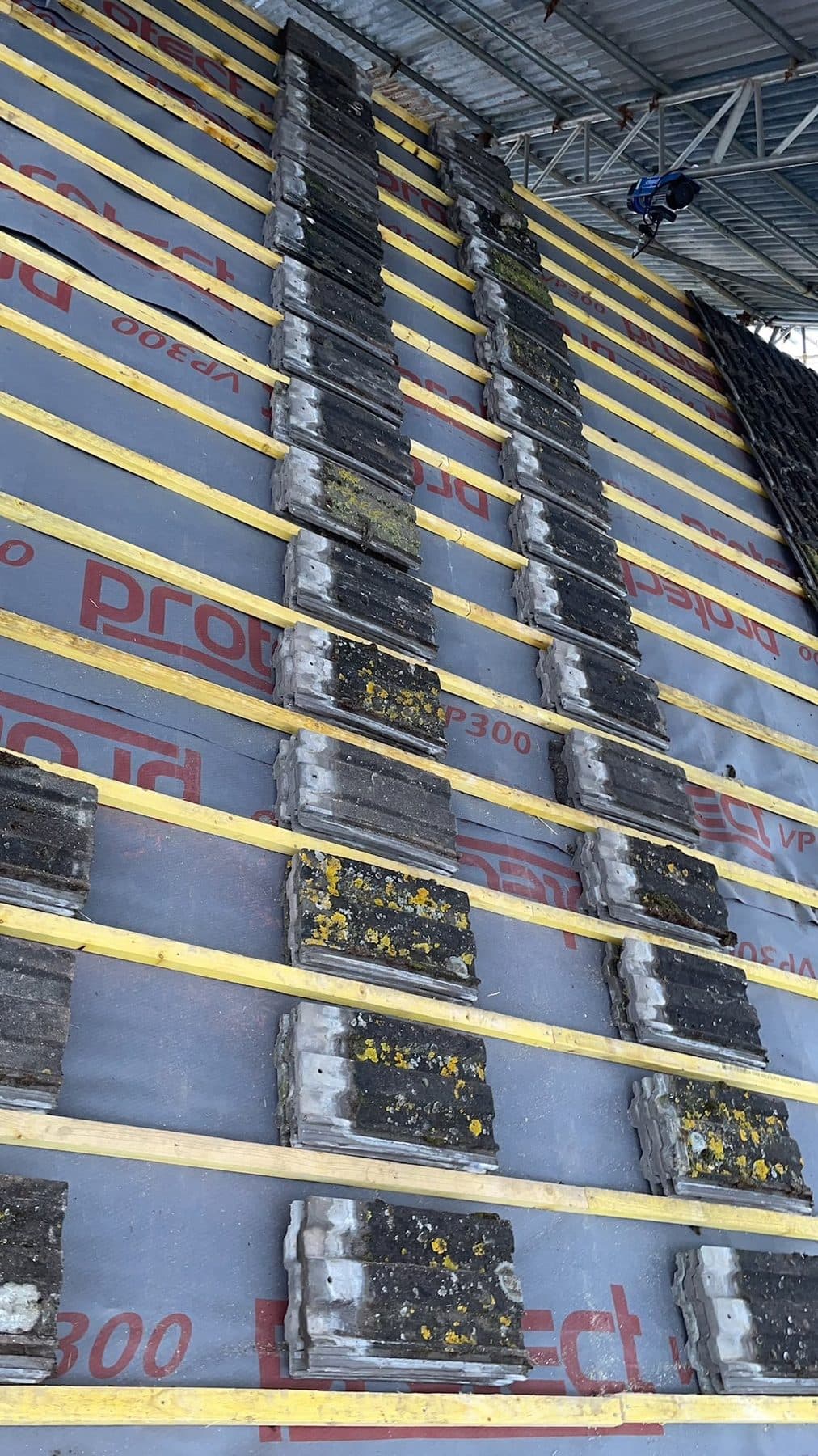 Old roof tiles stacked in rows on new battens and membrane under a scaffold roof